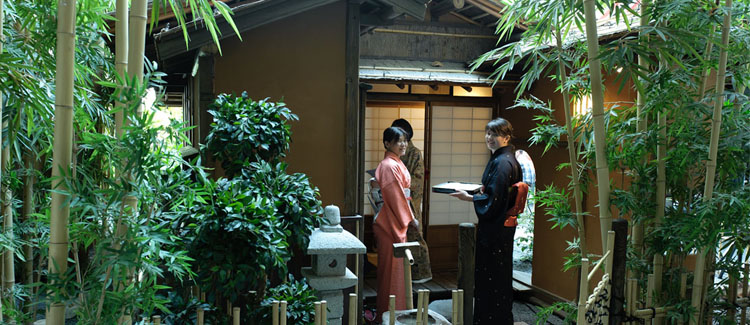 Two traditionally Japanese dressed women are standing in front of a teahouse.