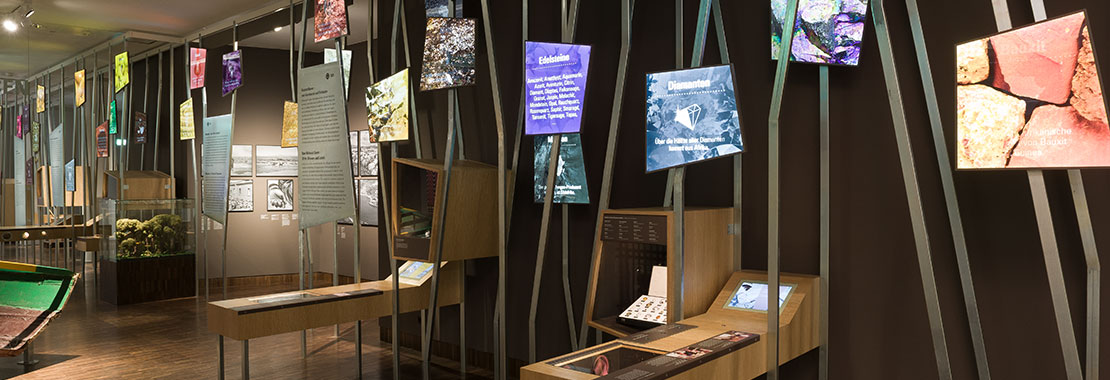 Blick in eine Ausstellung. An Metalstangen sind leuchtende Bild- und Texttafeln angebracht